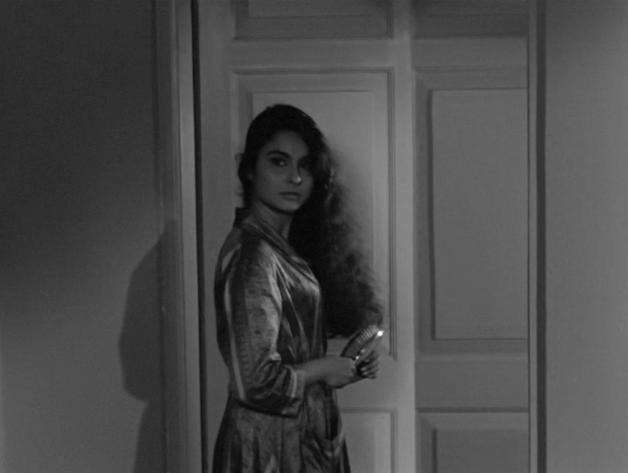 The Coward (1965) movie still: medium — A woman stands in a simple interior doorway against a plain wall. She looks toward the camera while holding…