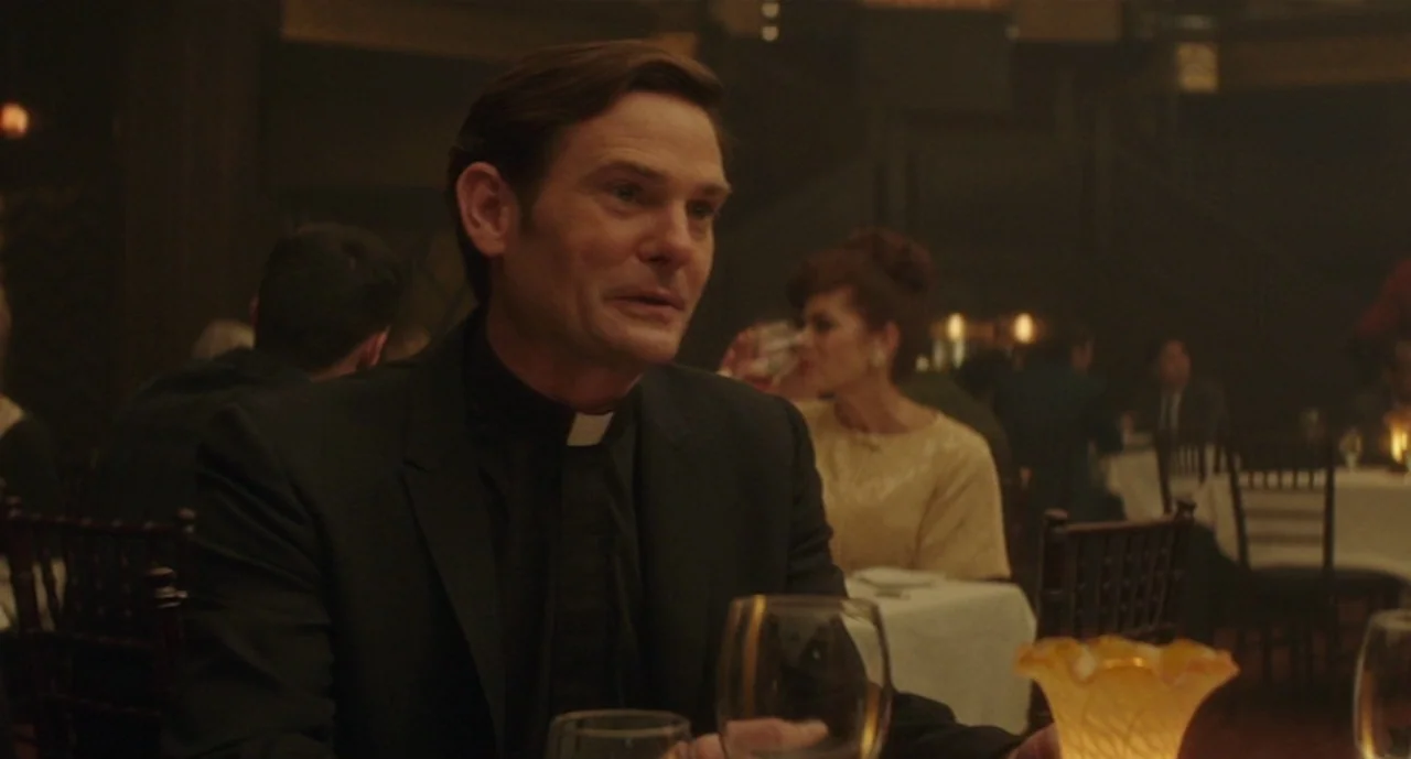 Ouija: Origin of Evil (2016) movie still: medium — A dimly lit restaurant has guests seated at tables with white tablecloths. A middle-aged priest…