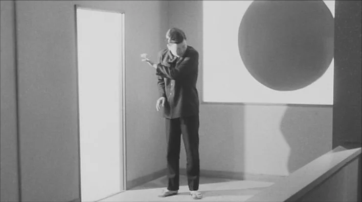 Death By Hanging (1968) movie still: fullbody — A minimalist white room features a rectangular doorway and a large circular mural element. A man in…