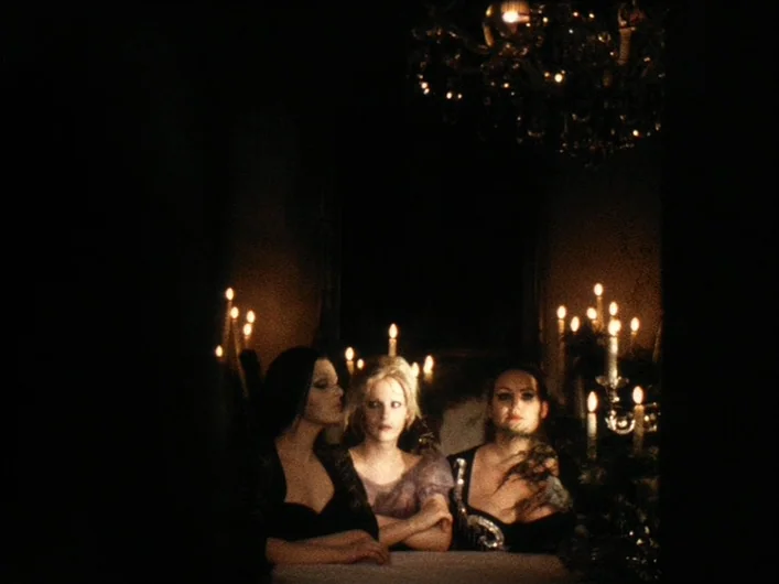 The Death of Maria Malibran (1972) movie still: medium — A dimly lit interior space features three women sitting together at a dark table. Multiple…
