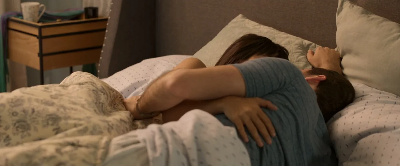 Tequila Re-Pasado (2023) movie still: medium — A residential bedroom contains a bed with patterned linens and an upholstered headboard. A man and a…