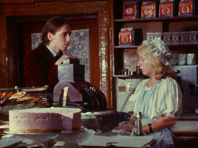 Der Bomberpilot (1970) movie still: medium — A small bakery interior features shelves stocked with boxes of Brandt rusks behind a counter. A man in…