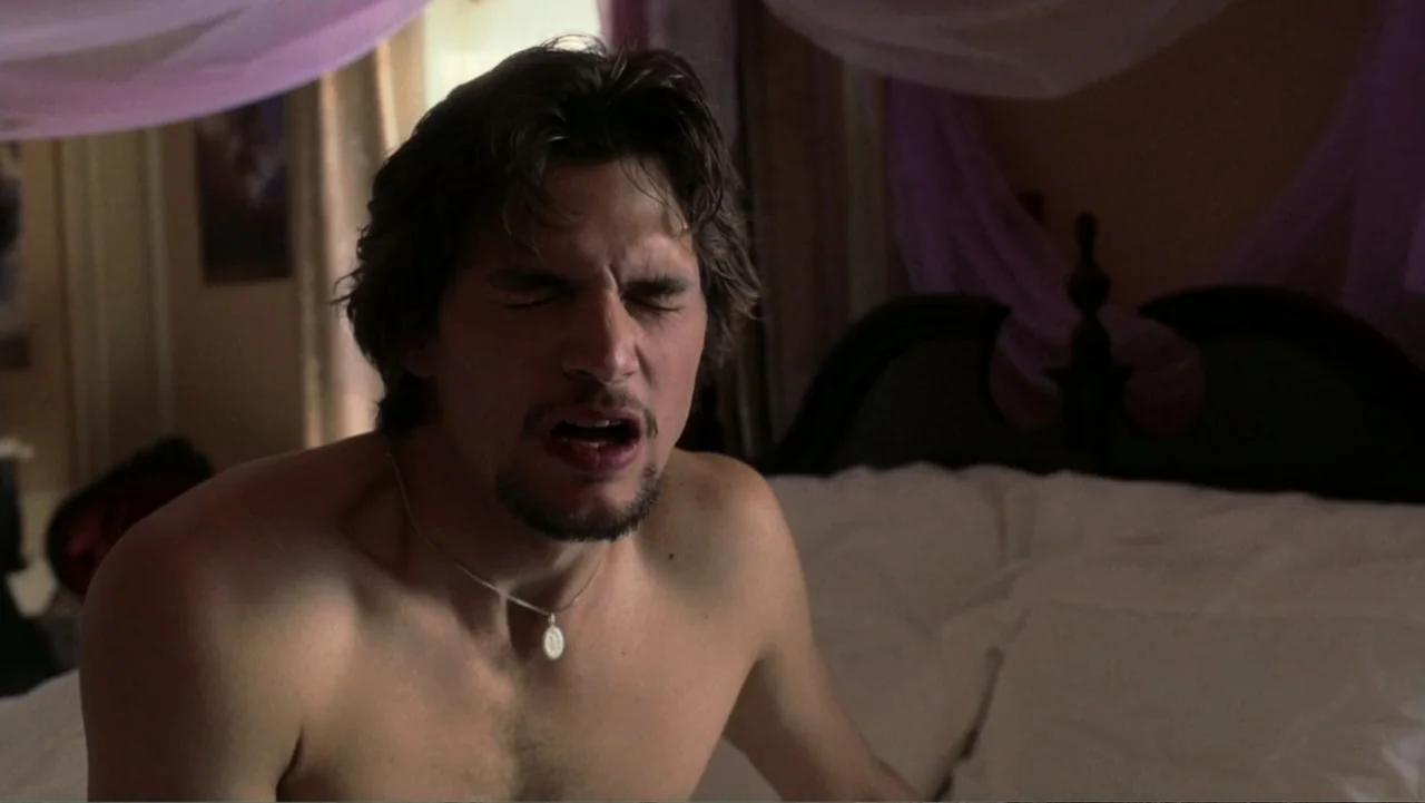 The Butterfly Effect (2004) movie still: medium — A well-lit bedroom features a bed with white linens and draped purple fabric overhead. A shirtless…
