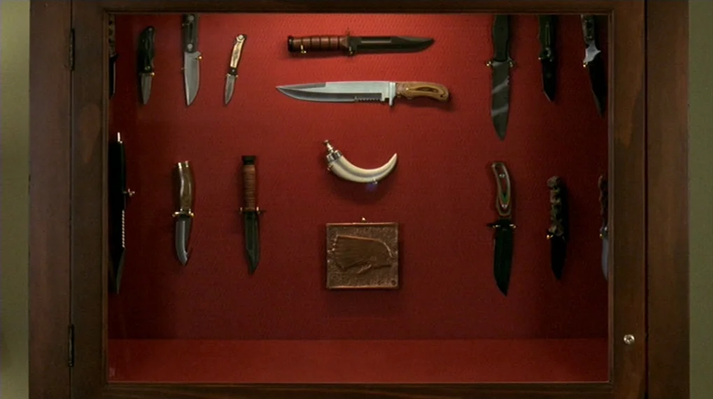 Year Of The Dog (2007) movie still: closeup — A wooden cabinet with a glass front features a red felt interior backdrop. Several hunting knives and…