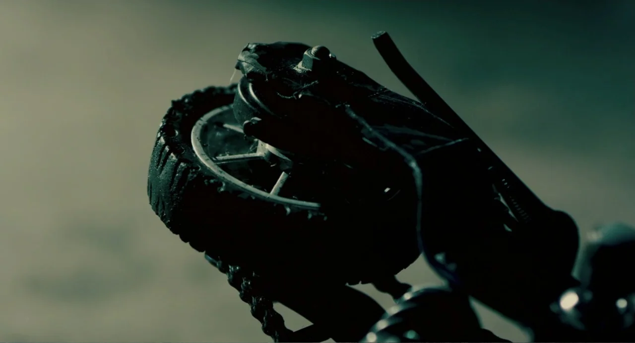 Terrifier (2018) movie still: closeup — A close-up view focuses on a damaged rubber tire and metallic mechanical part. The object is covered in…