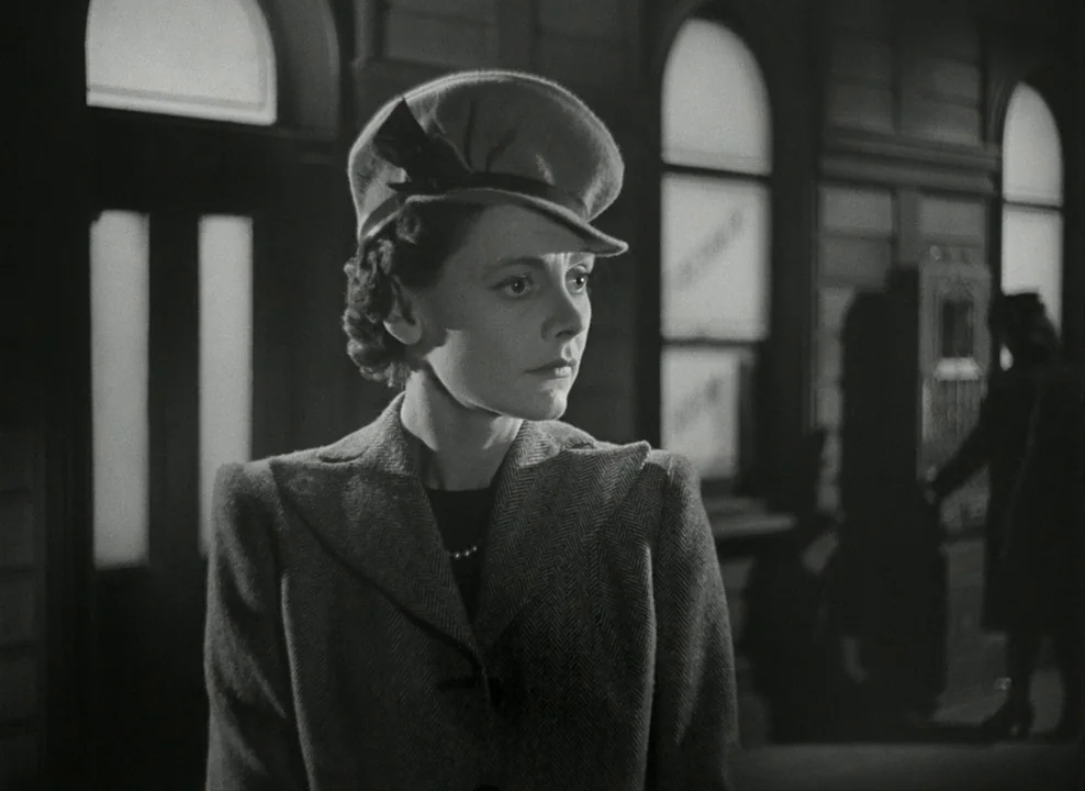 Brief Encounter (1945) movie still: medium — A dimly lit passenger terminal features arched windows in the background. A woman in a structured…