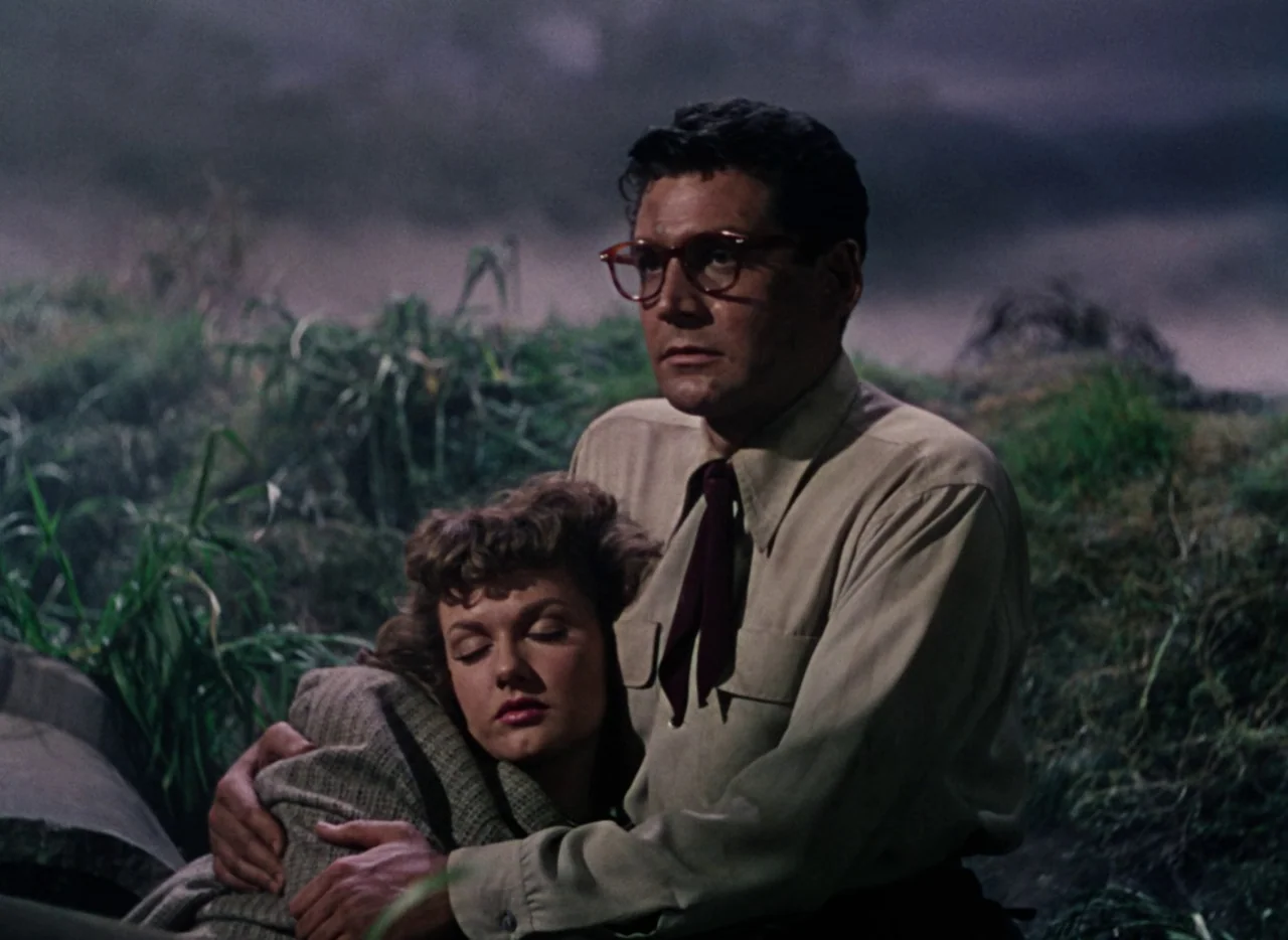 The War of the Worlds (1953) movie still: medium — A dark, grassy landscape at night provides the backdrop for two people. A man holding a woman in…