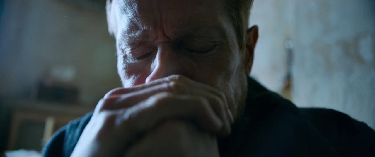 At Eternity’s Gate (2018) movie still: closeup — An interior space with muted walls and minimal background detail. A man with his eyes closed…