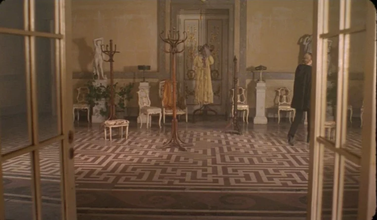 The Turn of the Century (2001) movie still: wide — A spacious hall features a geometric Greek key floor pattern and neoclassical decor. A man in a…