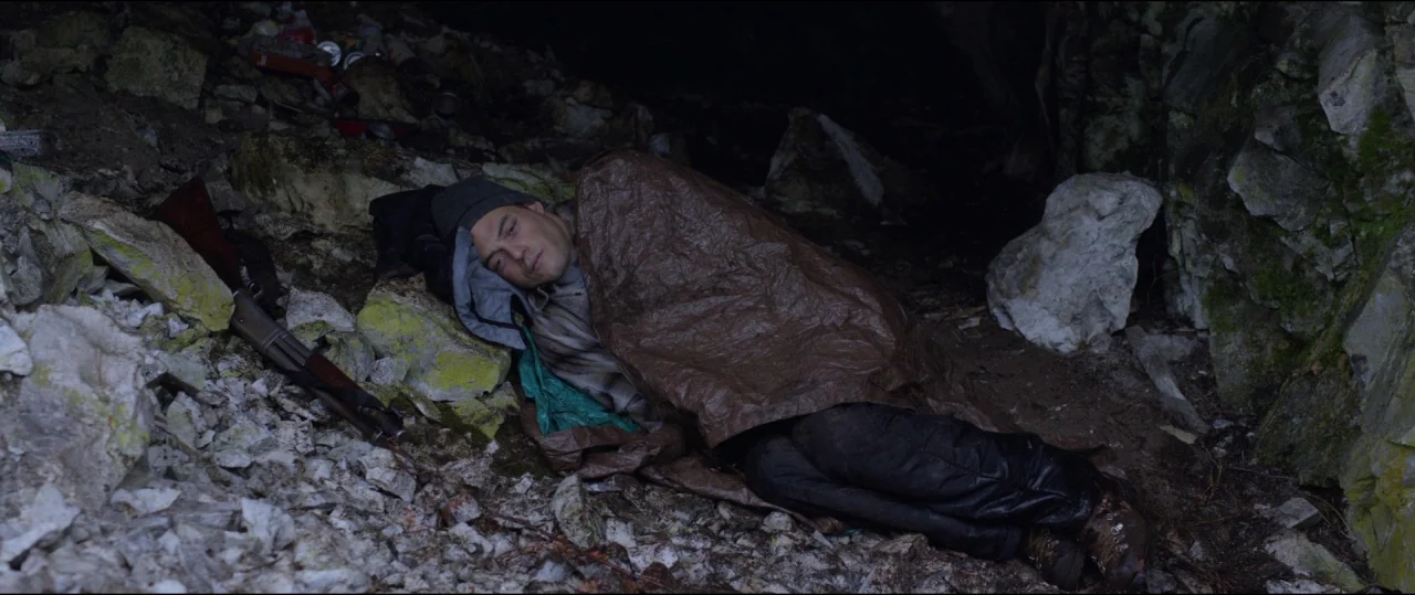 Buster’s Mal Heart (2016) movie still: medium — A dark cave interior with rough rock walls and a floor covered in loose rubble. A man lies on the…
