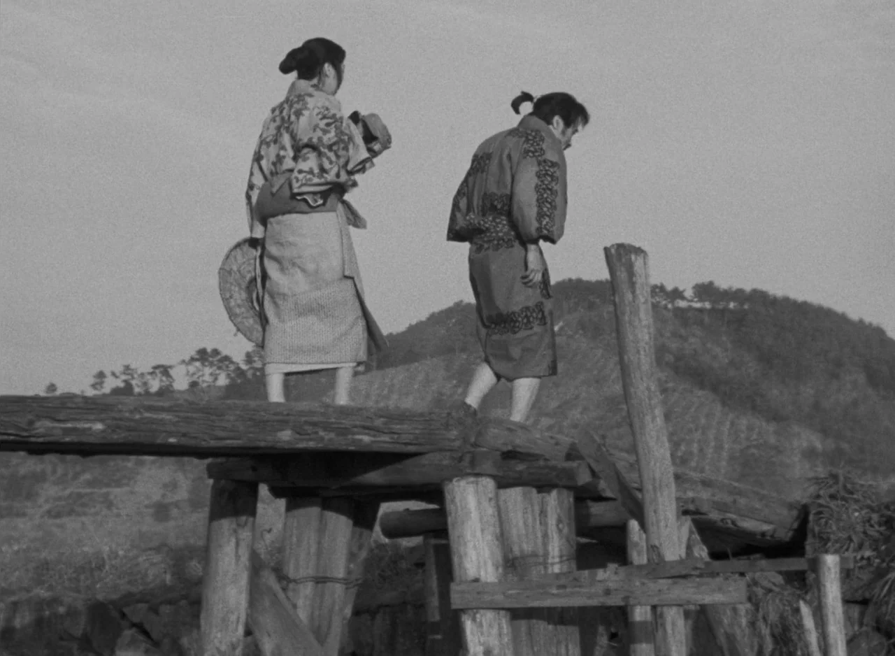 Ugetsu (1953) movie still: fullbody — A rustic wooden bridge crosses over an unseen depression in a rural landscape. A man and a woman walk away…