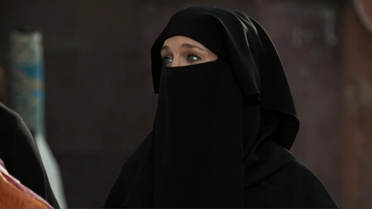 Sex and the City 2 (2010) movie still: closeup — A woman wears a black niqab against a blurred dark brown textured background. The subject is…