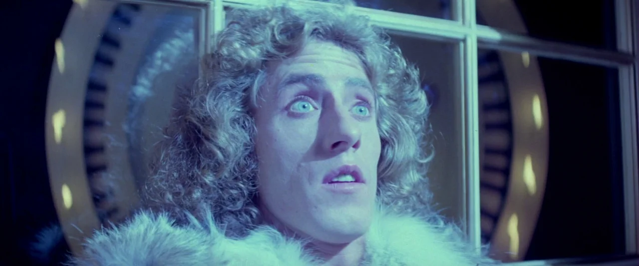 Lisztomania (1975) movie still: closeup — A man stands before a large circular architectural frame in a dark space. He looks upward with a wide-eyed…