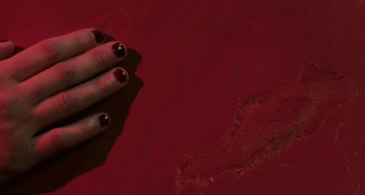 Bastards (2013) movie still: closeup — A close-up view shows a person's hand resting on a worn, textured red surface. The material shows signs of…