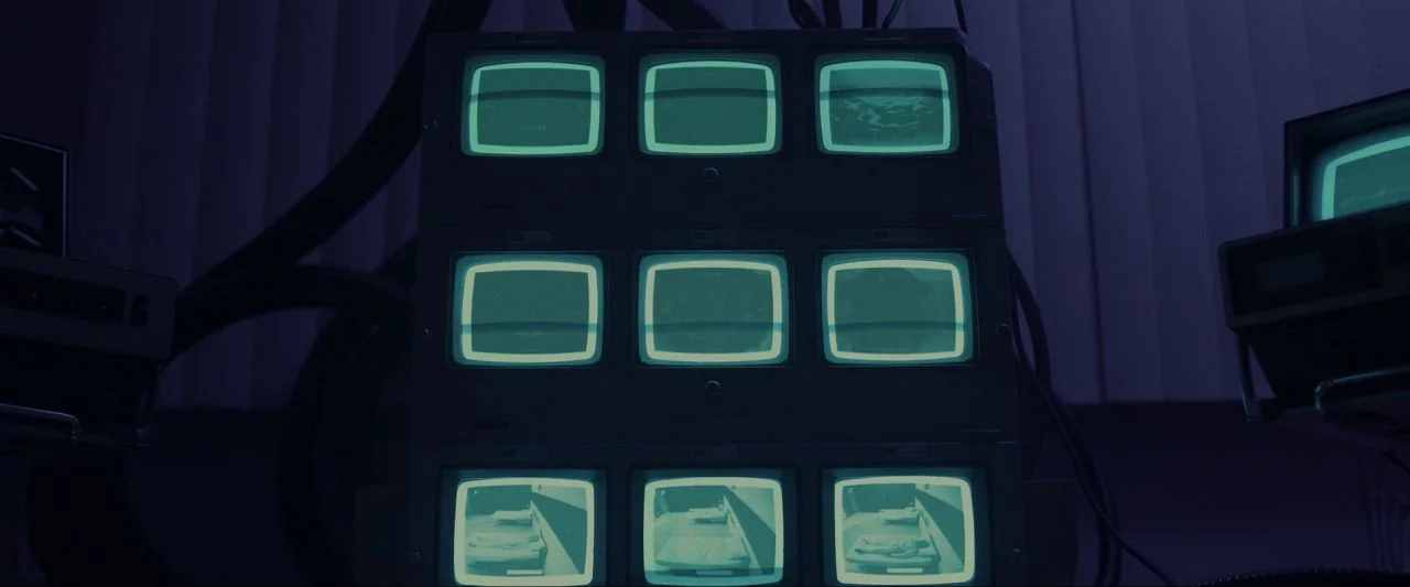 Come True (2020) movie still: medium — A dark room contains a central stack of nine vintage television monitors. The screens emit a pale cyan light…