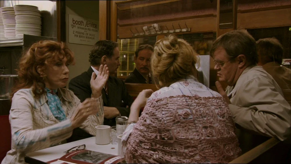 A Prairie Home Companion movie still: medium — An interior of a vintage American diner featuring wood paneling and booth seating arrangements. A…