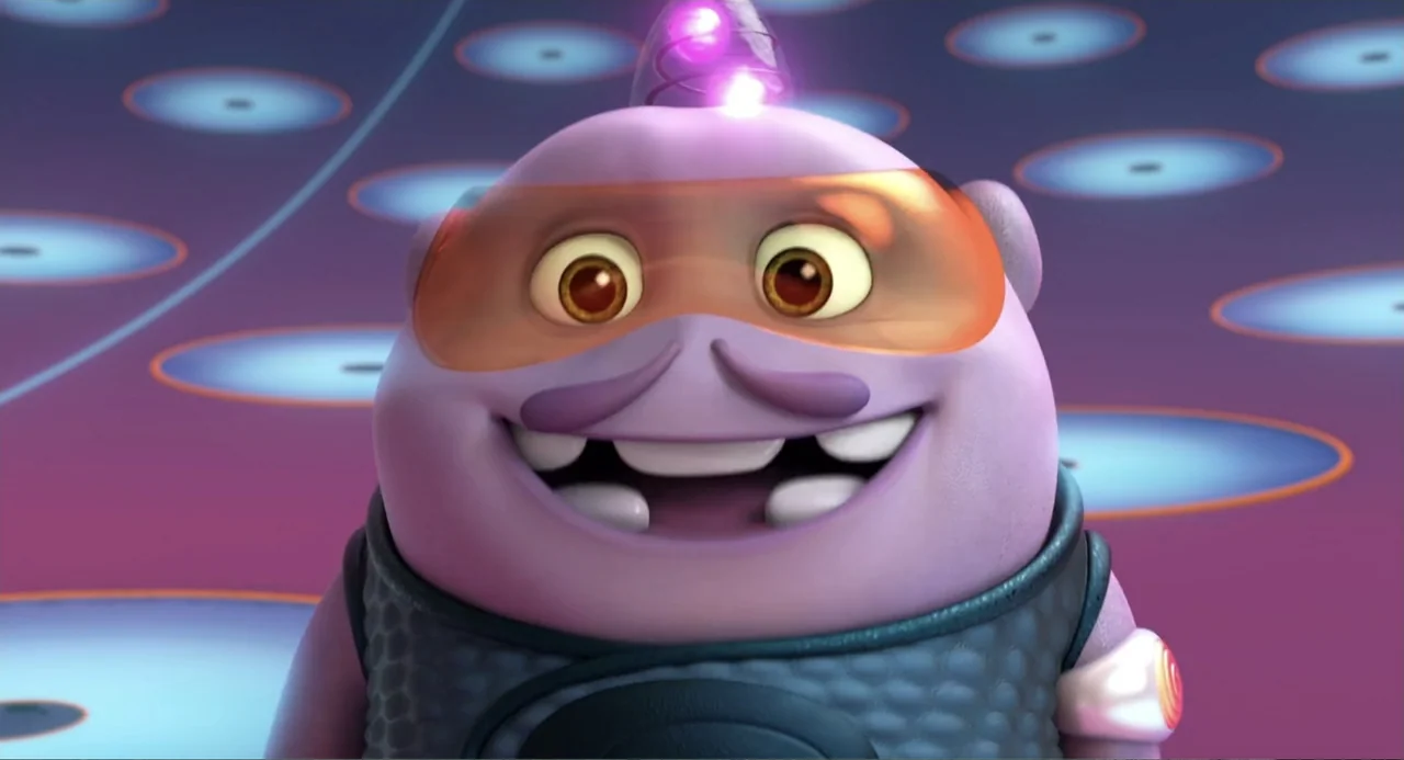 Home (2015) movie still: closeup — A cartoon purple alien character occupies a dimly lit room with glowing floor circles. The alien smiles widely…