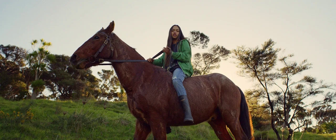 Hunt for the Wilderpeople (2016) movie still: fullbody — A grassy hilly pasture with sparse native trees stands under a clear late afternoon sky. A…
