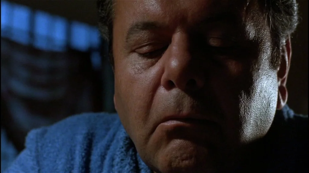 Goodfellas (1990) movie still: closeup — An older man sits in a dim room with blue ambient light hitting his face. The subject rests with his eyes…