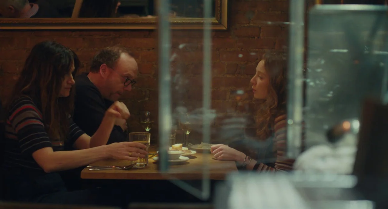 Private Life (2018) movie still: medium — A restaurant booth with exposed brick walls and a wooden dining table. Three people are seated around the…