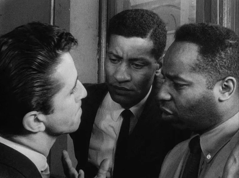 Shadows (1958) movie still: closeup — Three men stand closely together in an indoor space with a window frame visible. The men appear to be in a…
