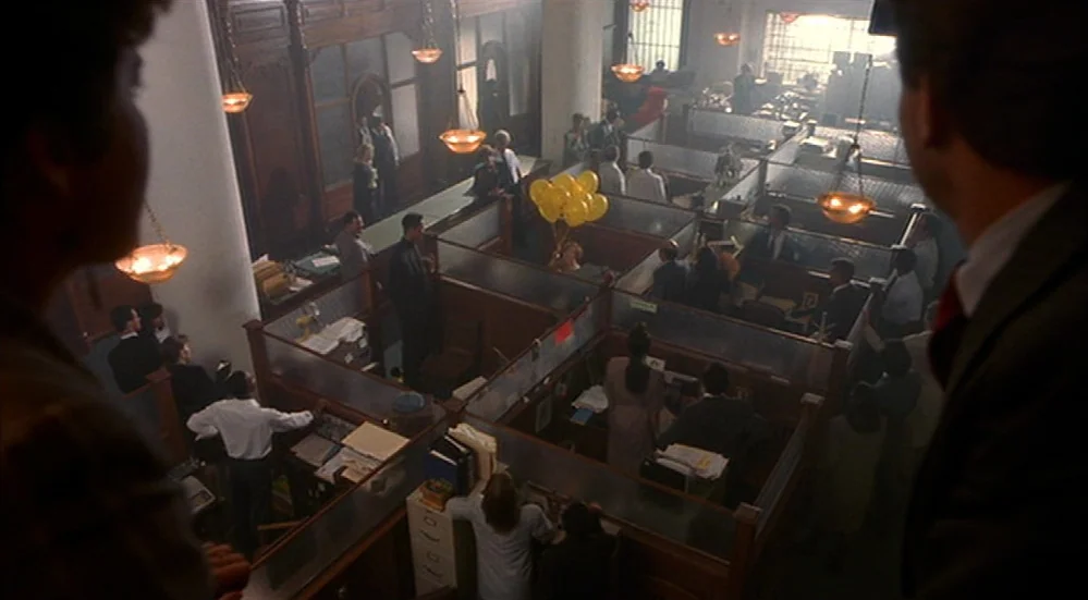 The Fisher King (1991) movie still: wide — A crowded corporate bullpen is filled with wood-partitioned cubicles and numerous employees at work. A…