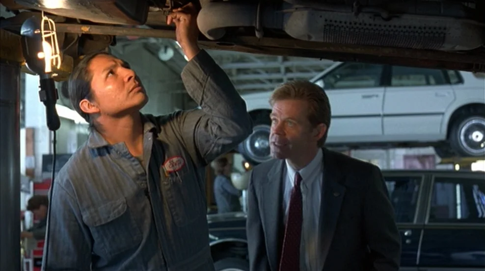 Fargo (1996) movie still: medium — An auto repair shop interior features cars elevated on lifts and fluorescent lighting. A mechanic in blue…