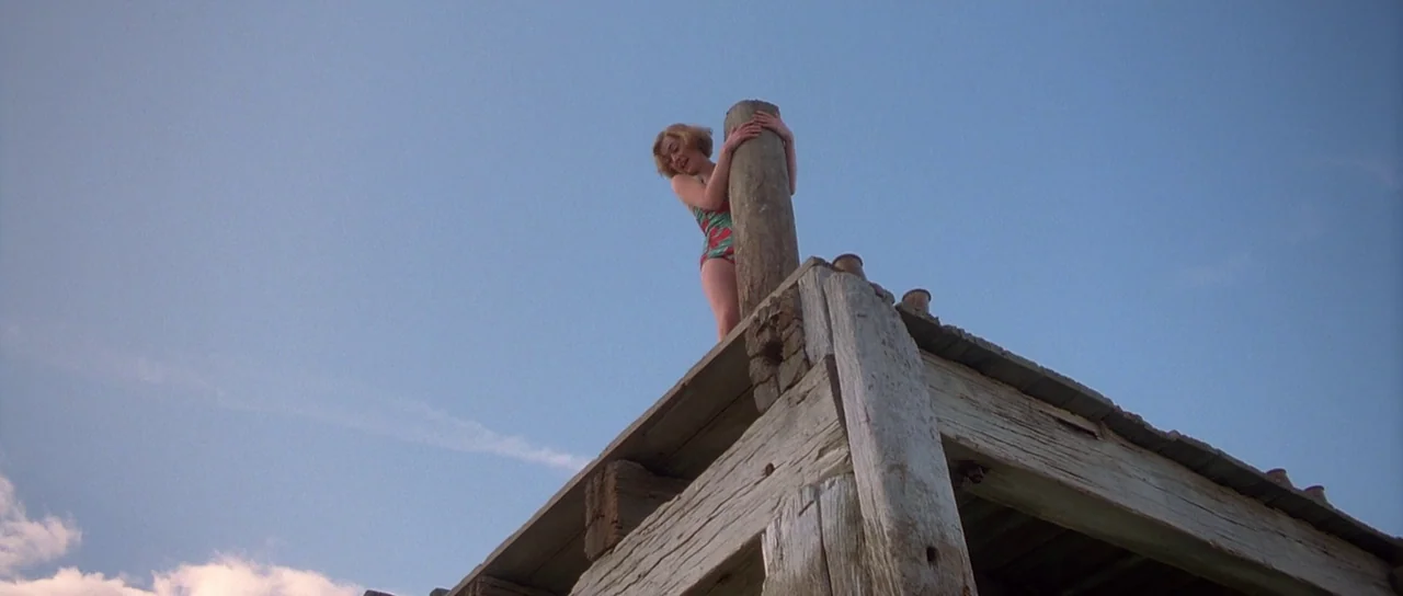 Heavenly Creatures (1994) movie still: medium — A weathered wooden platform structure sits against a clear blue sky. A young woman stands on the…