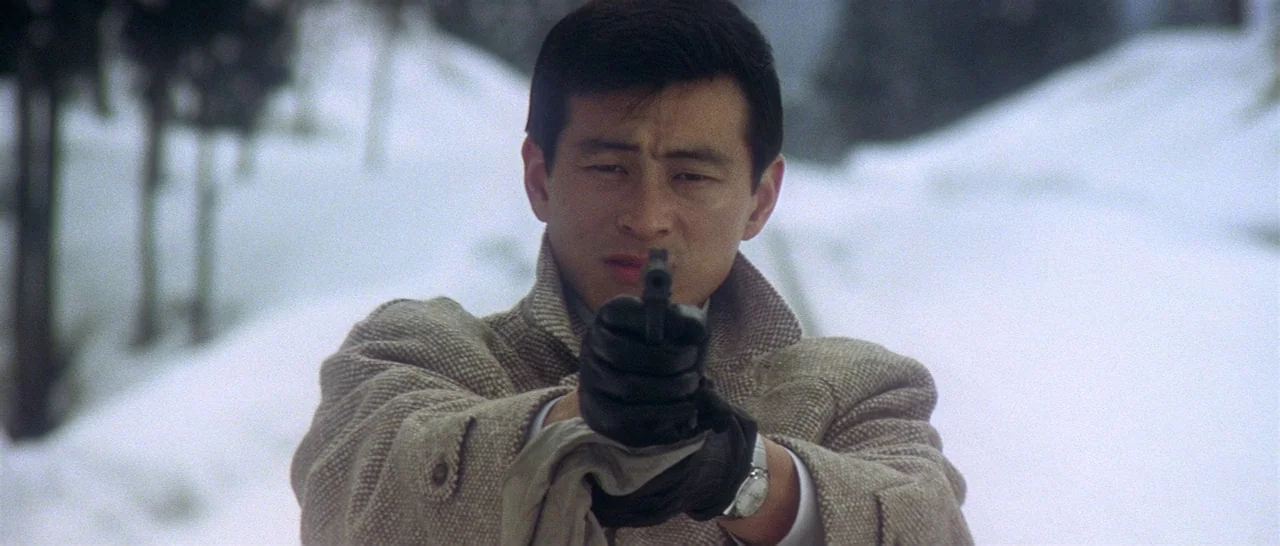 Tokyo Drifter (1966) movie still: medium — A man stands in a vast, snow-covered landscape with sparse trees in the background. The man holds a…