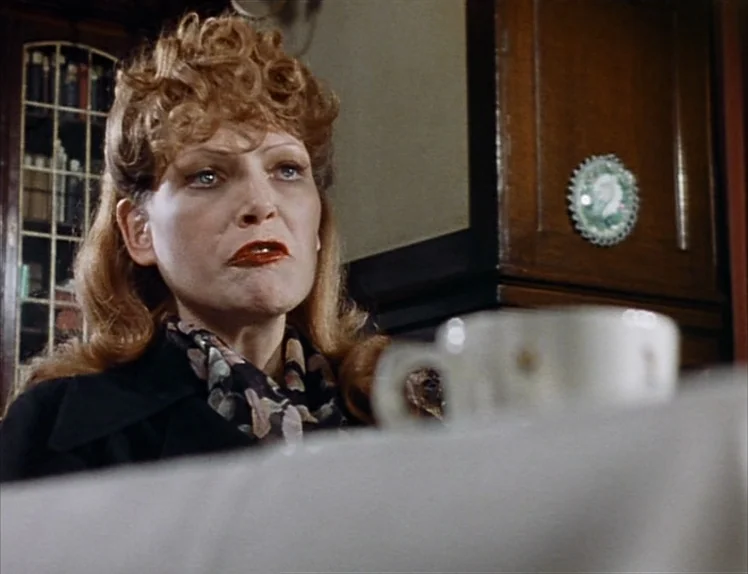 Martha (1974) movie still: medium — A woman sits at a table in a room with wood paneling. She looks forward while a white coffee cup sits in the…
