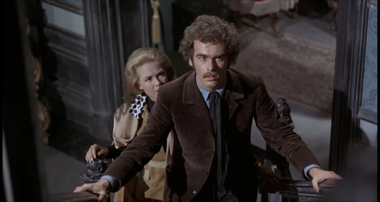The Dunwich Horror (1970) movie still: medium — A wooden staircase interior with ornate banisters and dark walls. A man leads a woman upstairs as…