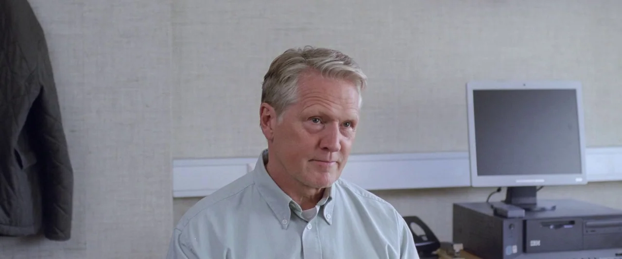 A White, White Day (2019) movie still: medium — A sterile office workspace with beige fabric walls and a modern computer monitor. An older man in a…
