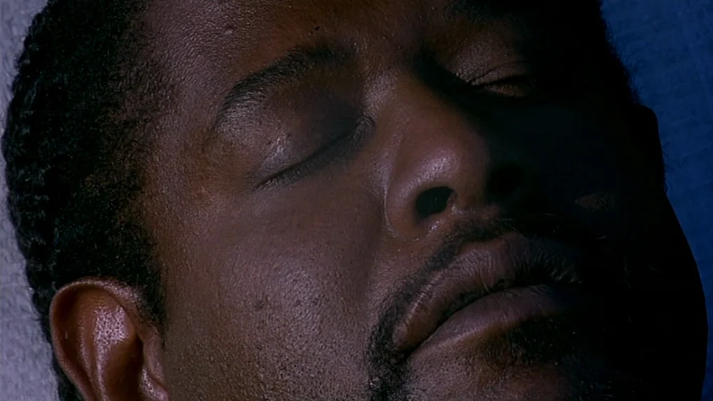 Ghost Dog: The Way of the Samurai (1999) movie still: closeup — An extreme close-up of a man's face against a dark, featureless background. The man…