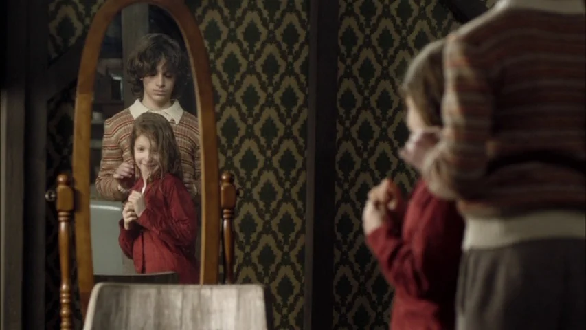The Sleeping Beauty (2010) movie still: Two children stand before a vintage oval mirror, an older boy carefully adjusting his younger sister's…