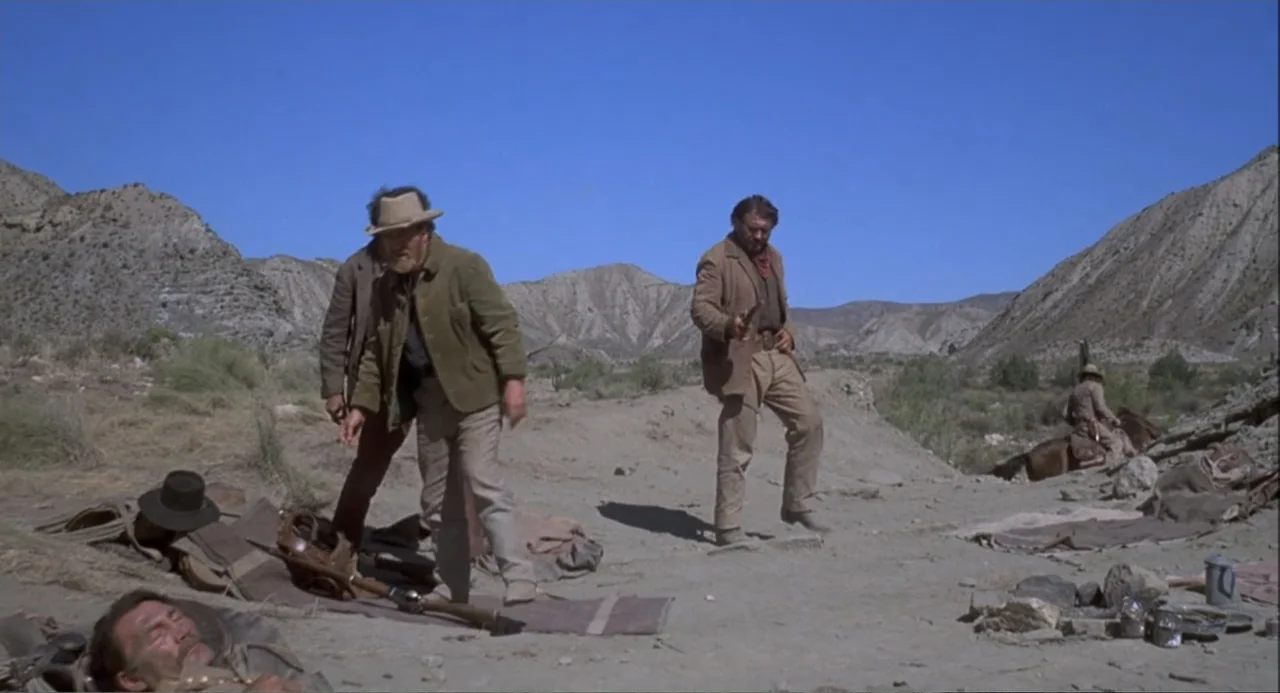 Chato's Land (1972) movie still: wide — An arid, rocky desert landscape stretches out beneath a clear, expansive blue sky. Several men move through…