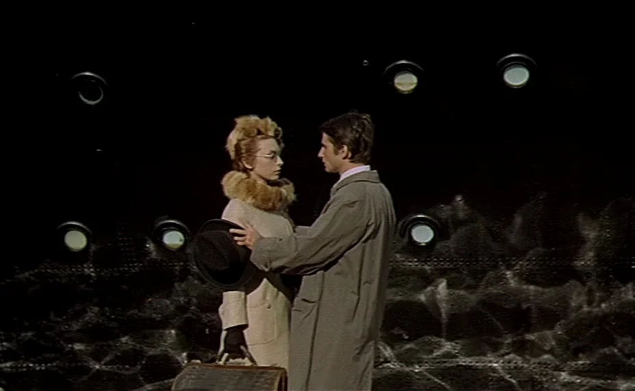 Two English Girls (1971) movie still: medium — Two individuals stand against a dark wall punctuated by circular, glowing light fixtures. They face…