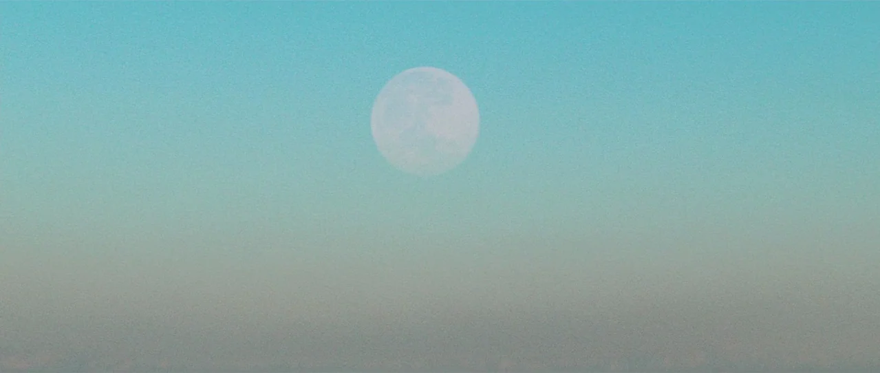 Biutiful (2010) movie still: establishing — A bright full moon hangs centered in a clear, gradient-filled evening sky. There are no other objects or…