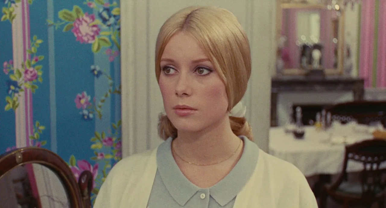 The Umbrellas Of Cherbourg (1964) movie still: closeup — A dining room featuring vibrant blue floral wallpaper and a table in the background. A…