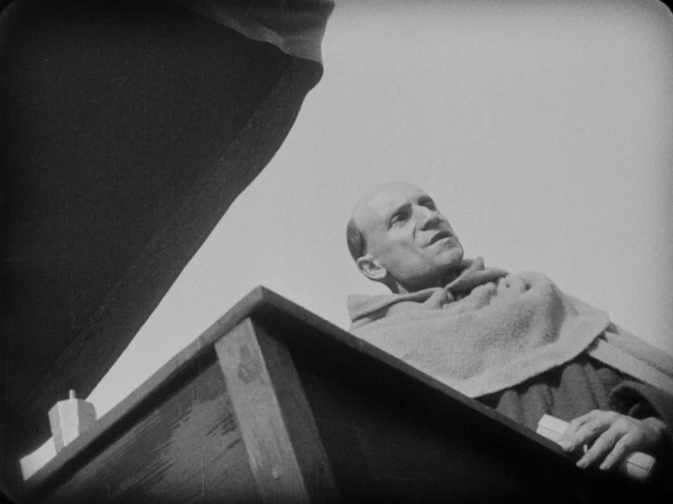 The Passion of Joan of Arc (1928) movie still: medium — A wooden pulpit structure sits against a bright, clear sky. A monk in a religious robe gazes…