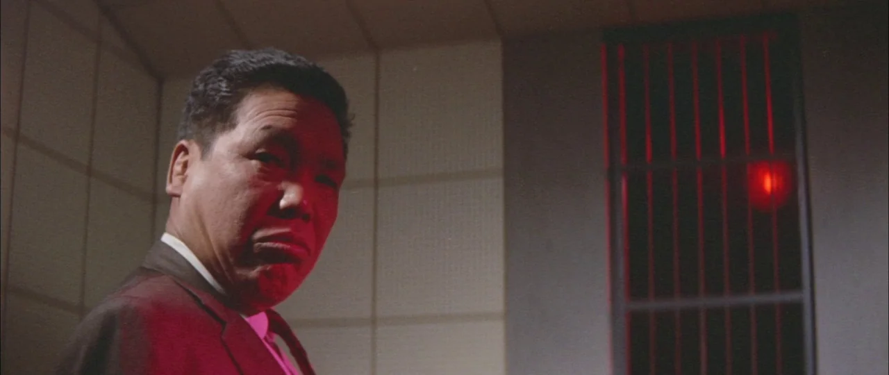Black Tight Killers (1966) movie still: medium — A dimly lit industrial hallway features tiled walls and a metal grate window. An Asian man stands…