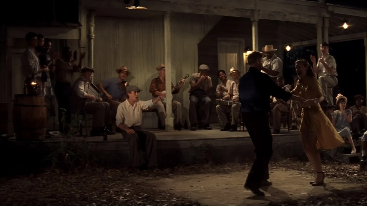 The Notebook (2004) movie still: fullbody — A wooden porch at night serves as a stage for a group of musicians. A couple dances on the dirt area in…