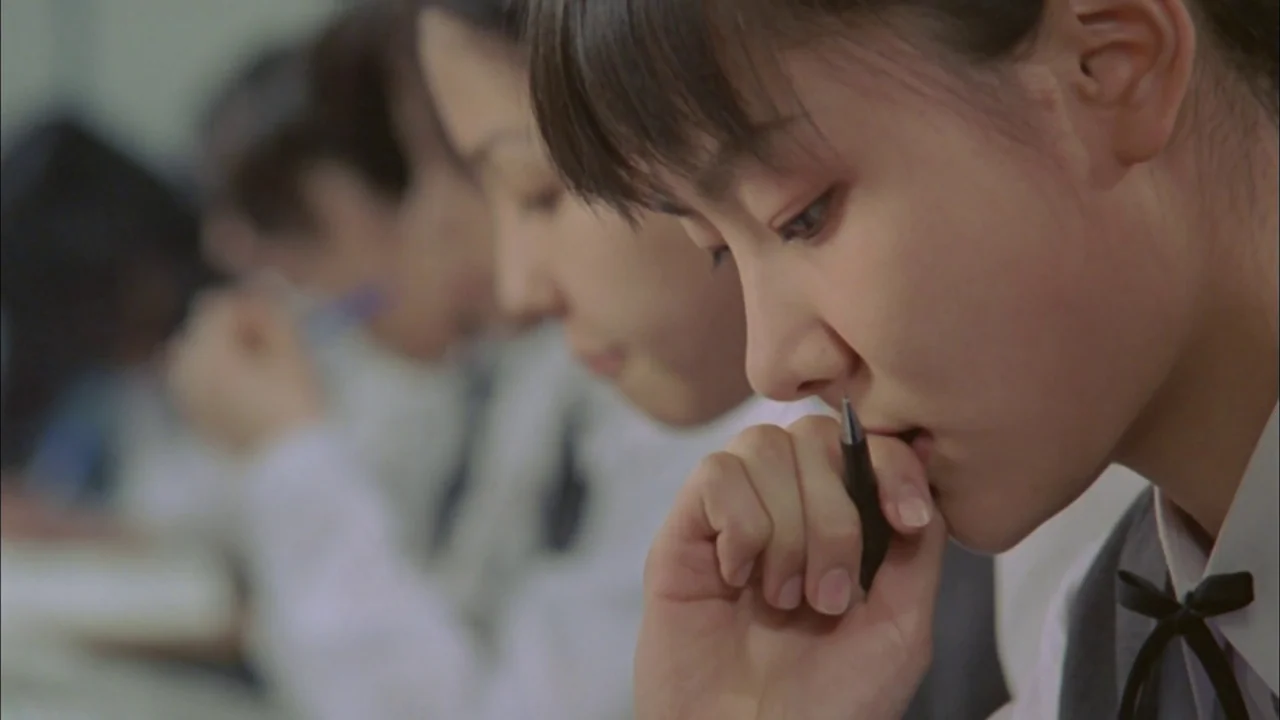 Whispering Corridors (1998) movie still: closeup — A rows-based educational setting with students seated in a brightly lit room. A student in the…
