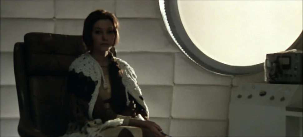 Solaris (1972) movie still: medium — A minimalist white cabin interior features padded walls and a circular porthole window. A young woman in a…
