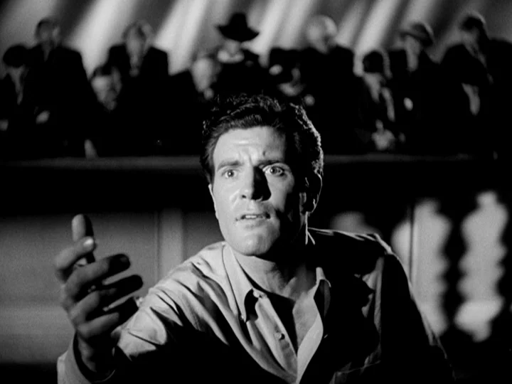 Stranger on the Third Floor (1940) movie still: medium — A dark, shadows-filled courtroom features a seated jury in the blurred background. A man…