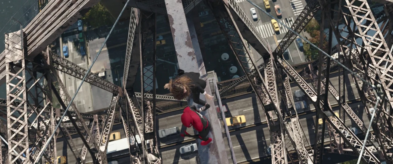Spider-Man: No Way Home (2021) movie still: wide — A top-down view shows a red-suited hero and a man crouching on a steel beam. Below them, traffic…