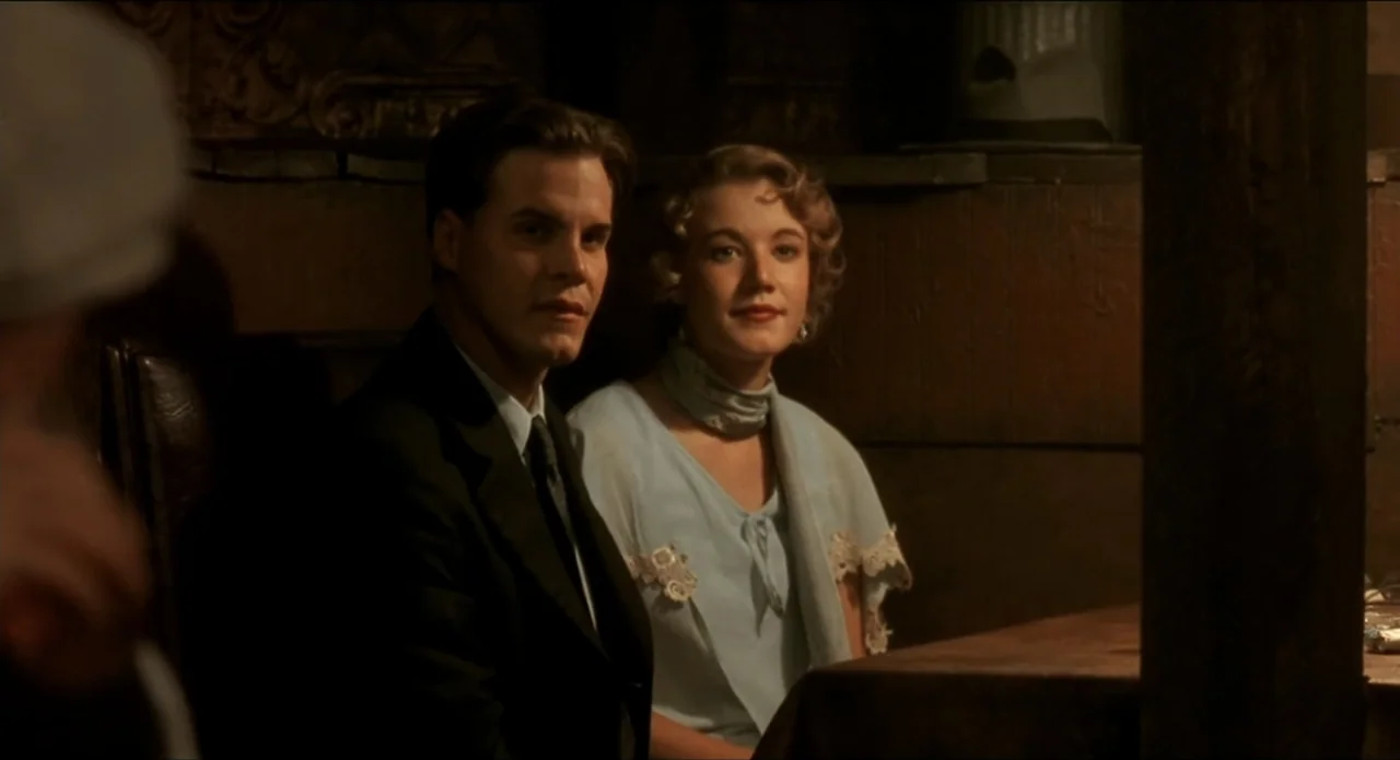 A River Runs Through It (1992) movie still: medium — A dimly lit indoor booth features a dark wood paneled wall and shadows. A man in a suit and a…