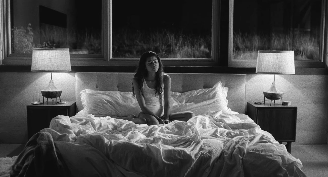 Malcolm & Marie (2021) movie still: medium — A modern bedroom features a large bed positioned directly in front of a wide window. A young woman in a…