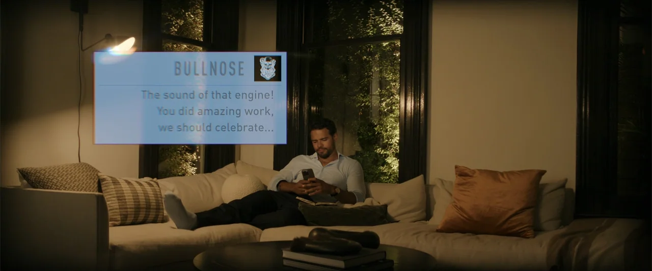 Maintenance Required (2025) movie still: medium — A dark living room features a modern beige sofa and two tall windows showing night foliage. A man…