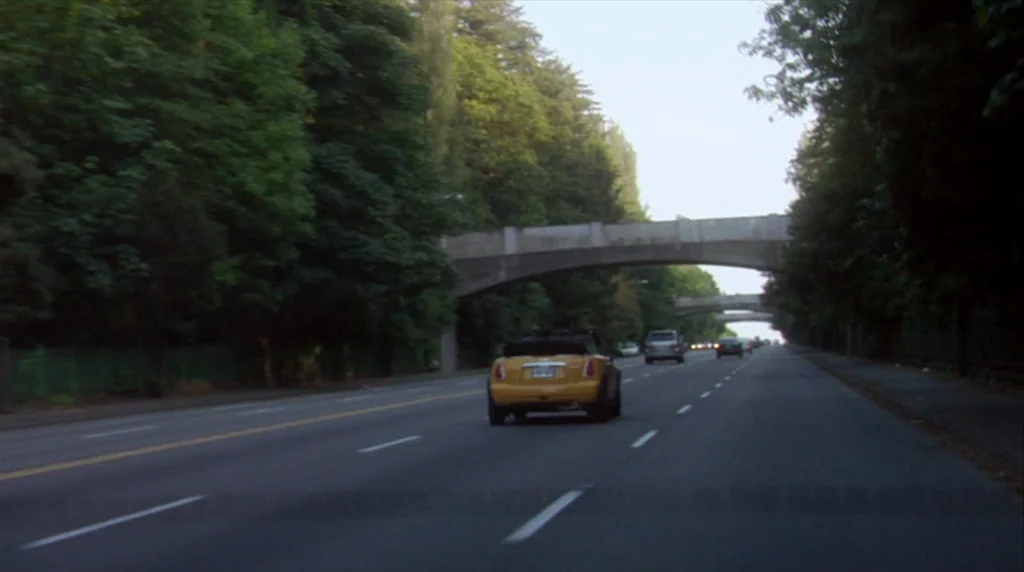 Humpday (2009) movie still: wide — A multi-lane road is lined with dense green trees and crossed by concrete bridges. Multiple cars travel along the…
