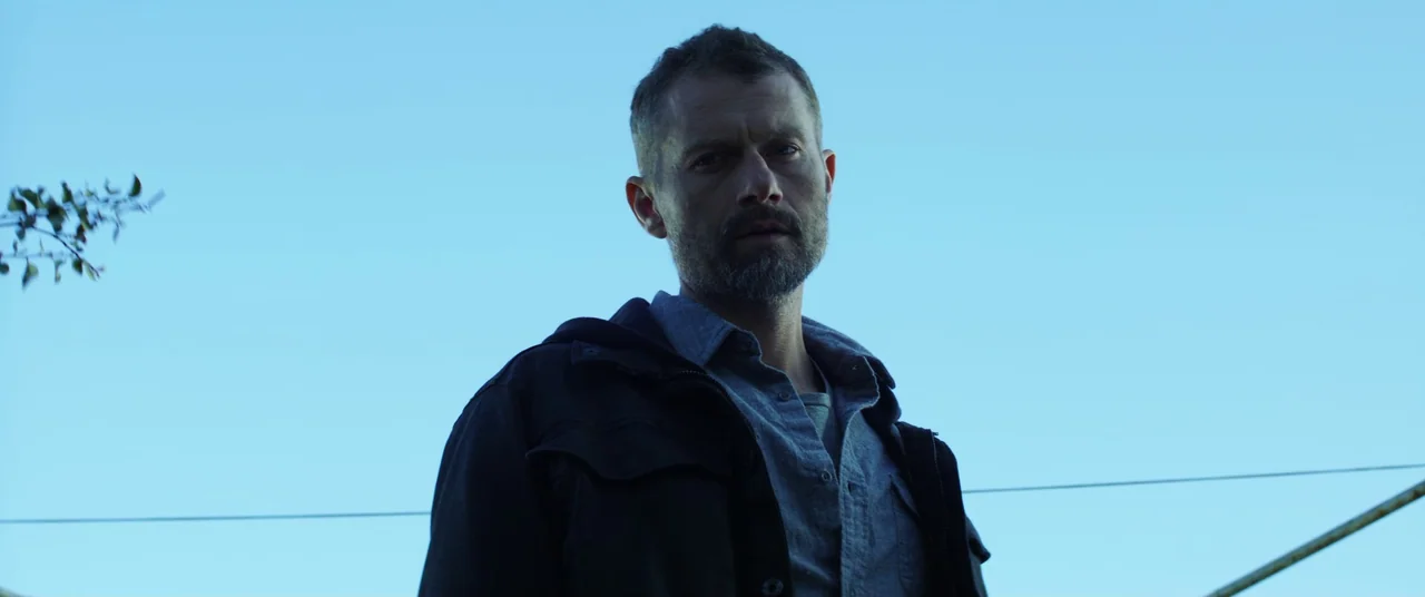 The Empty Man (2020) movie still: medium — An outdoor setting is dominated by a clear, bright blue sky. A man stands framed against the expansive…